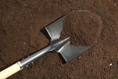 Photo of Metal shovel on fertile soil, top view. Gardening tool
