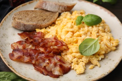 Photo of Delicious scrambled eggs with bacon and basil in plate on table, closeup