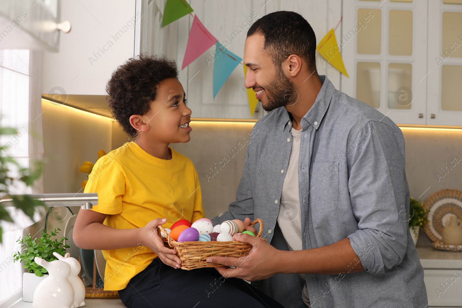 Photo of Happy African American father and his cute son with Easter eggs in kitchen