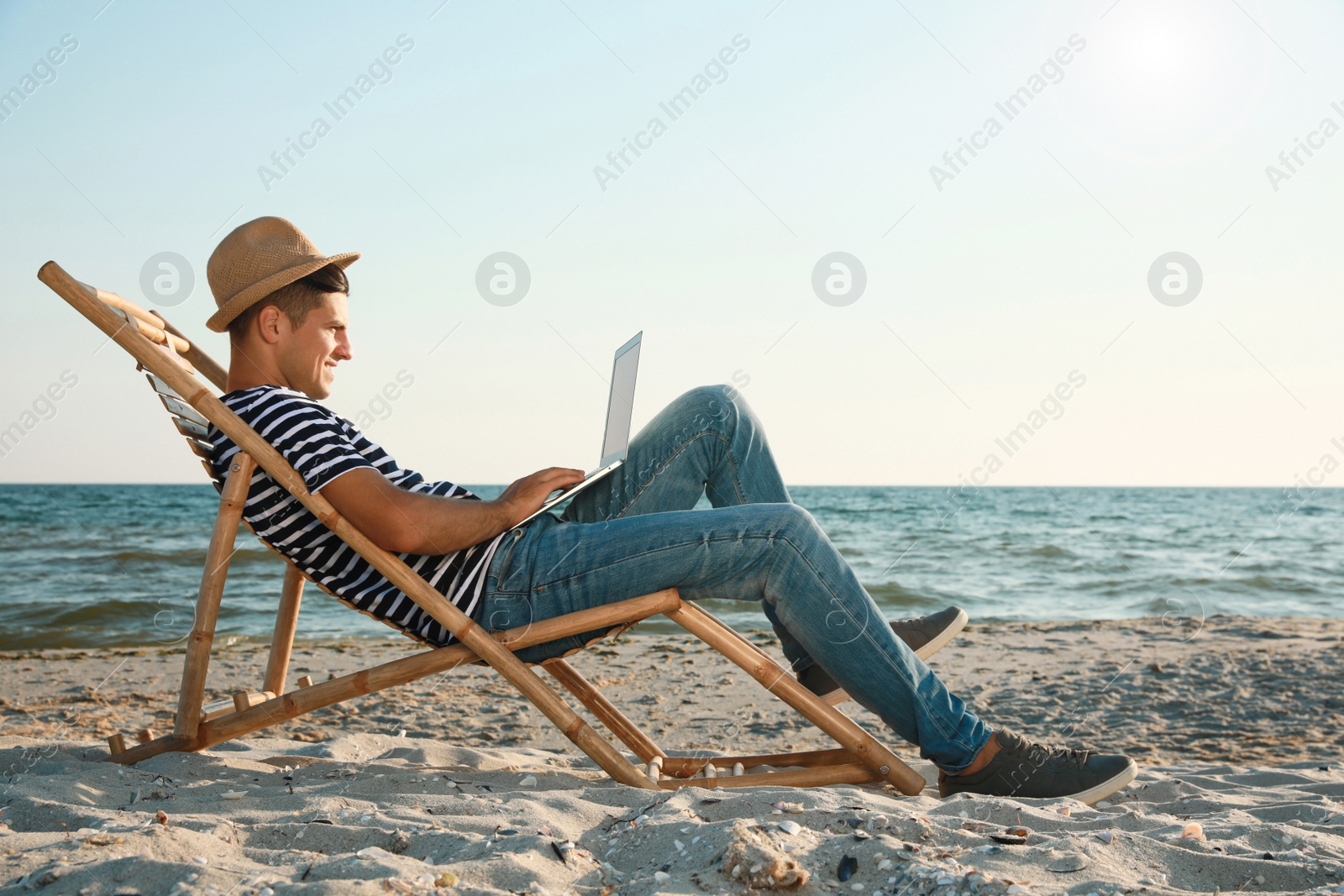 Photo of Man working with laptop in deck chair on beach