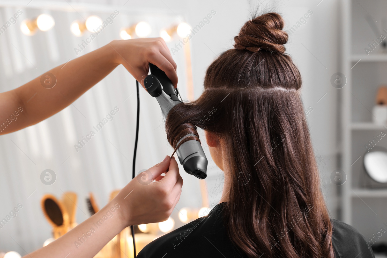 Photo of Hairdresser using curling hair iron while working with woman in salon, closeup