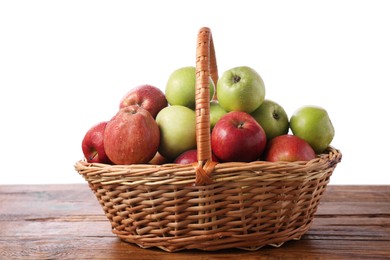 Fresh red and green apples in wicker basket on wooden table against white background