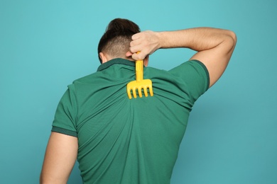 Photo of Young man scratching back with toy rake on color background. Annoying itch