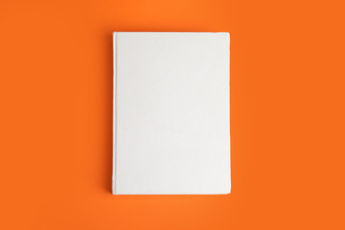 Book with blank cover on orange background, top view