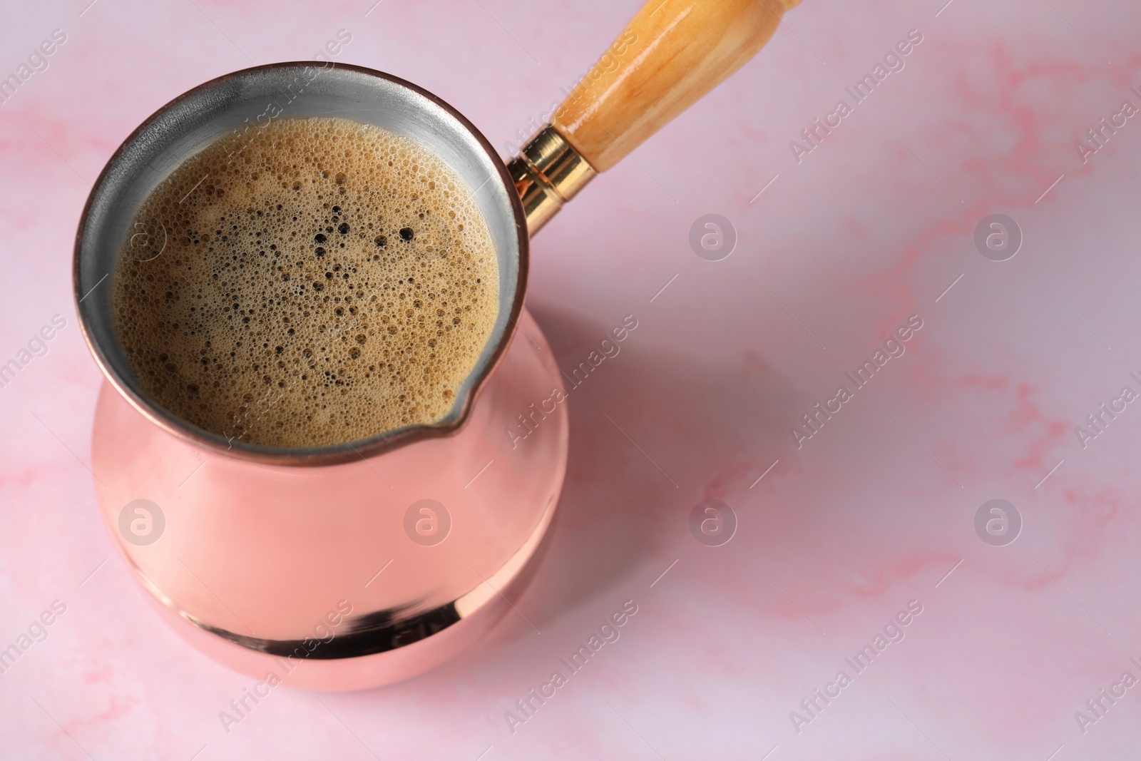 Photo of Turkish coffee in cezve on pink marble table. Space for text