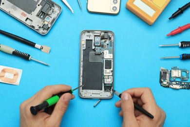 Man repairing broken smartphone on light blue background, top view