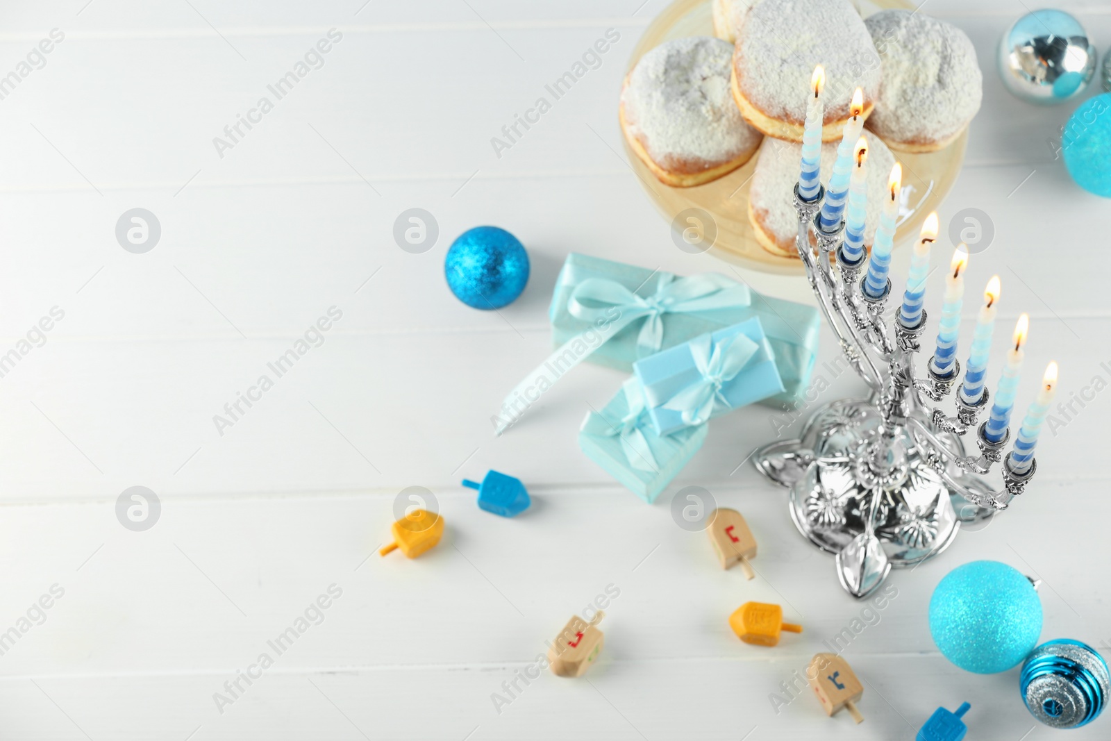 Photo of Composition with Hanukkah menorah, dreidels and gift boxes on white wooden table, above view. Space for text