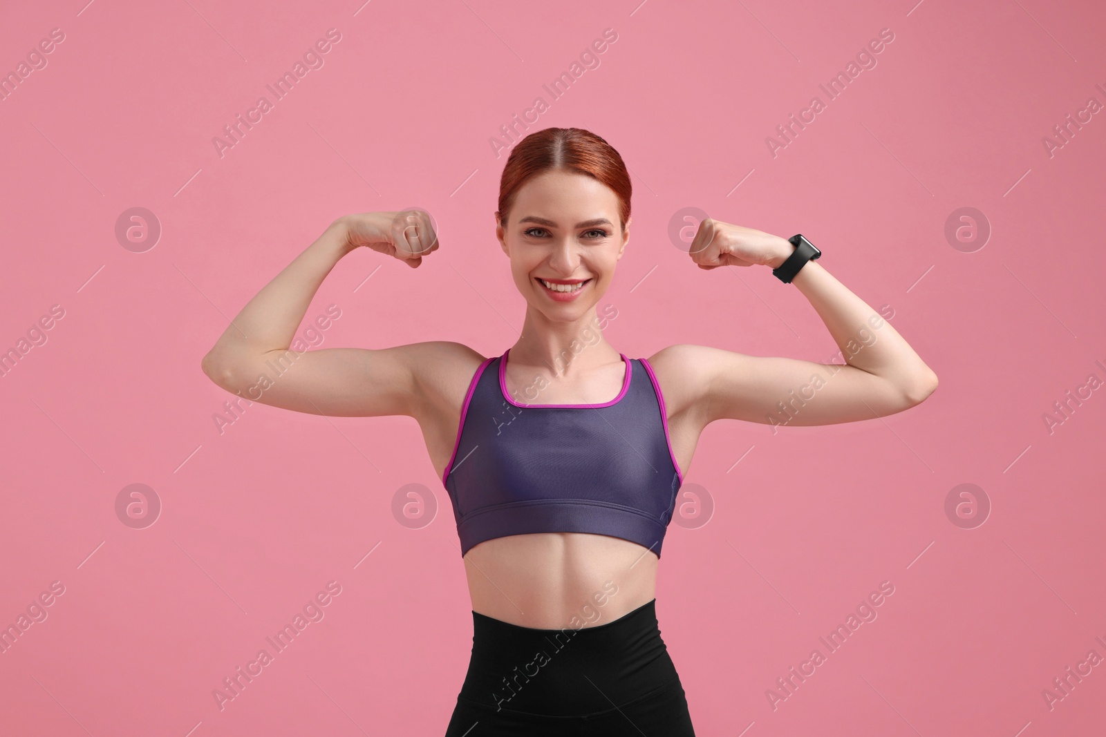 Photo of Young woman in sportswear showing muscles on pink background