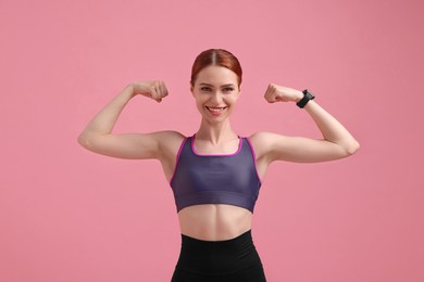 Photo of Young woman in sportswear showing muscles on pink background