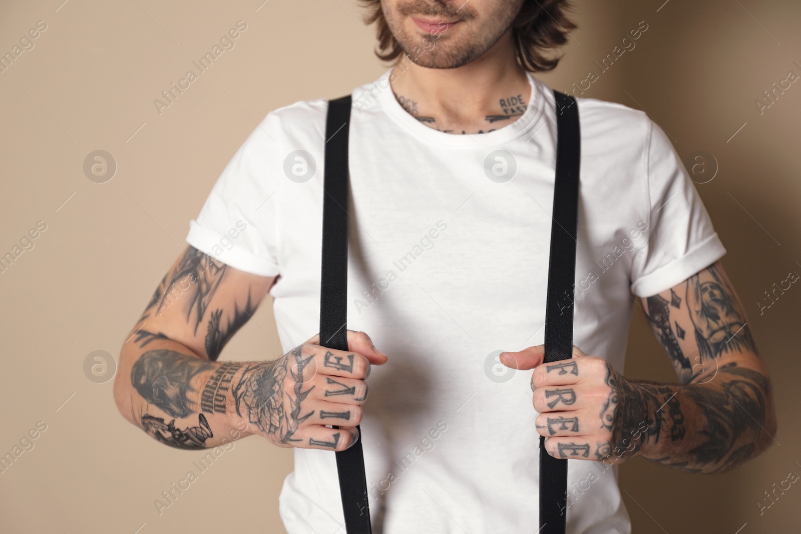 Photo of Young man with tattoos on arms against beige background, closeup