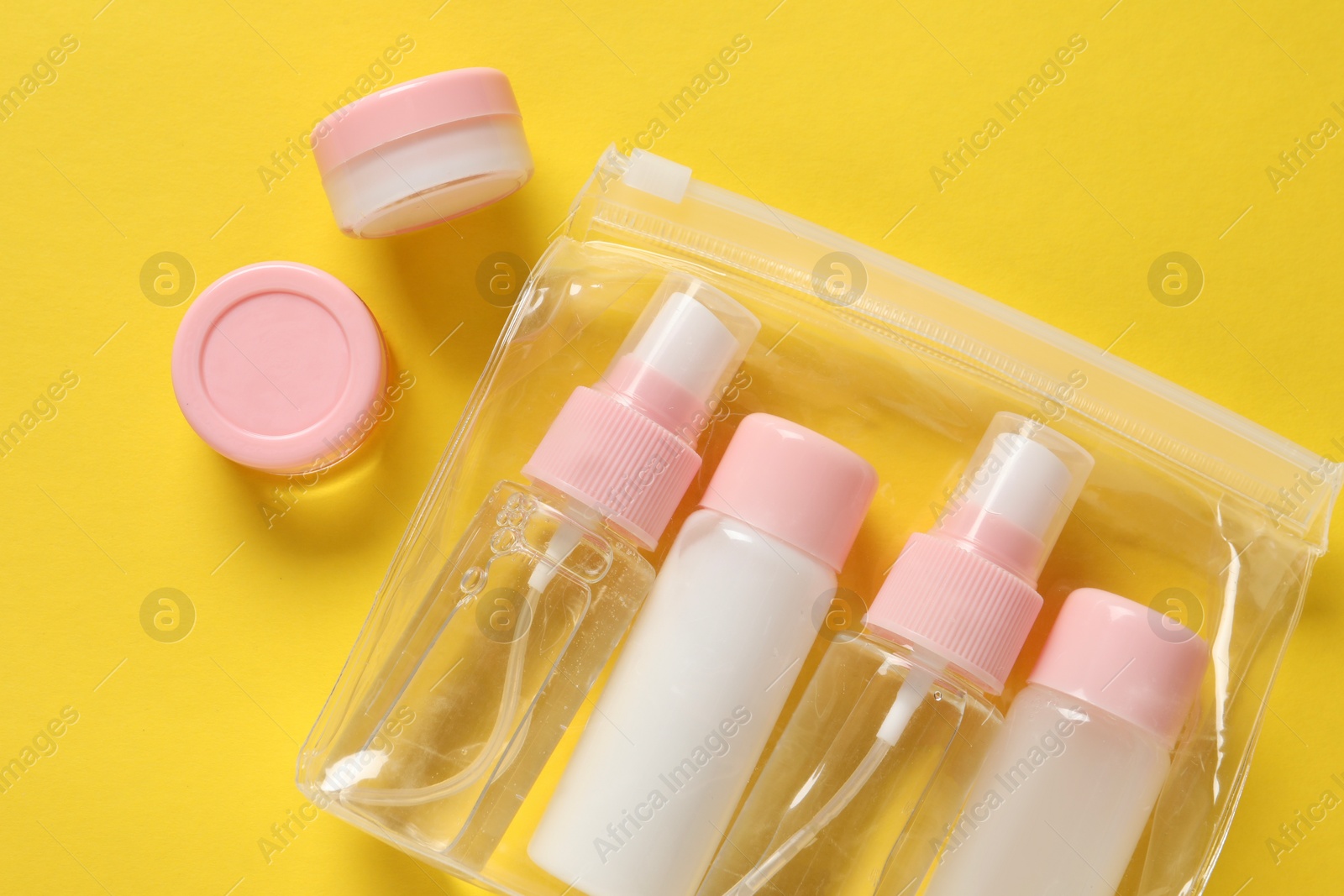 Photo of Plastic bag with cosmetic travel kit on yellow background, flat lay. Bath accessories