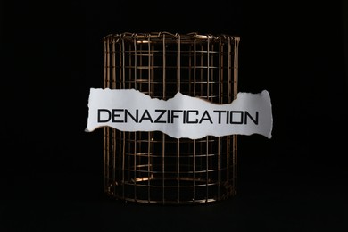 Photo of Paper with word Denazification and golden cage on black background