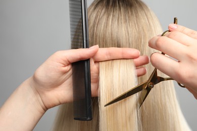 Photo of Hairdresser cutting client's hair with scissors on light grey background, closeup