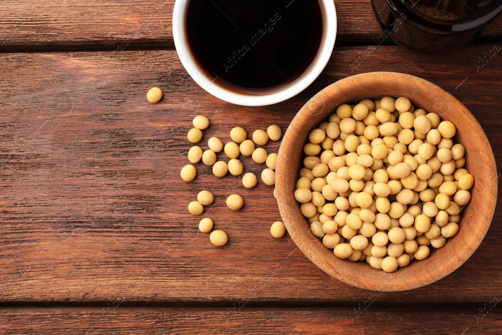 Photo of Soy sauce in bowl and soybeans on wooden table, flat lay. Space for text