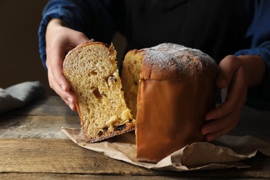 Woman taking slice of delicious Panettone cake with powdered sugar at wooden table, closeup. Traditional Italian pastry