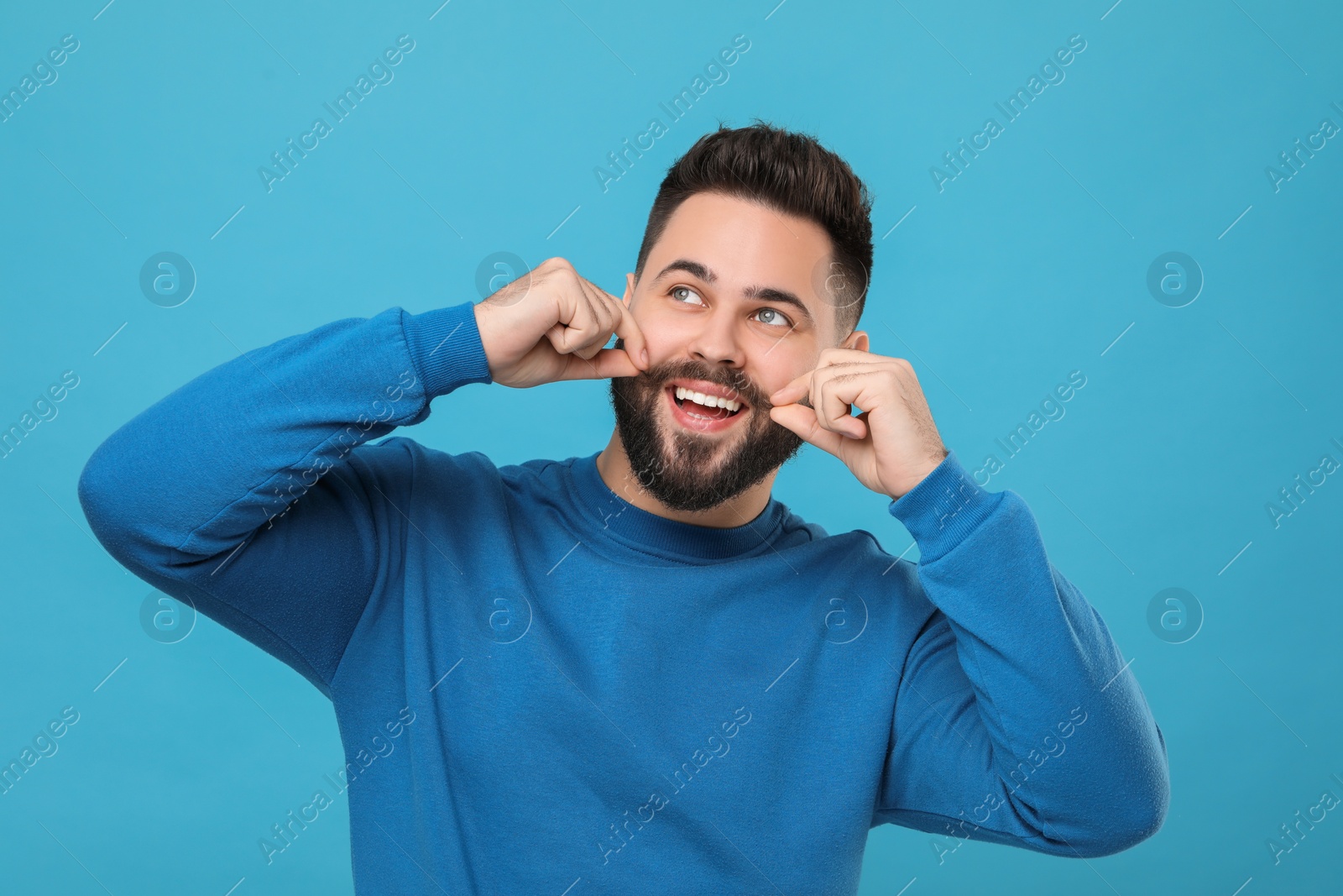 Photo of Happy young man touching mustache on light blue background