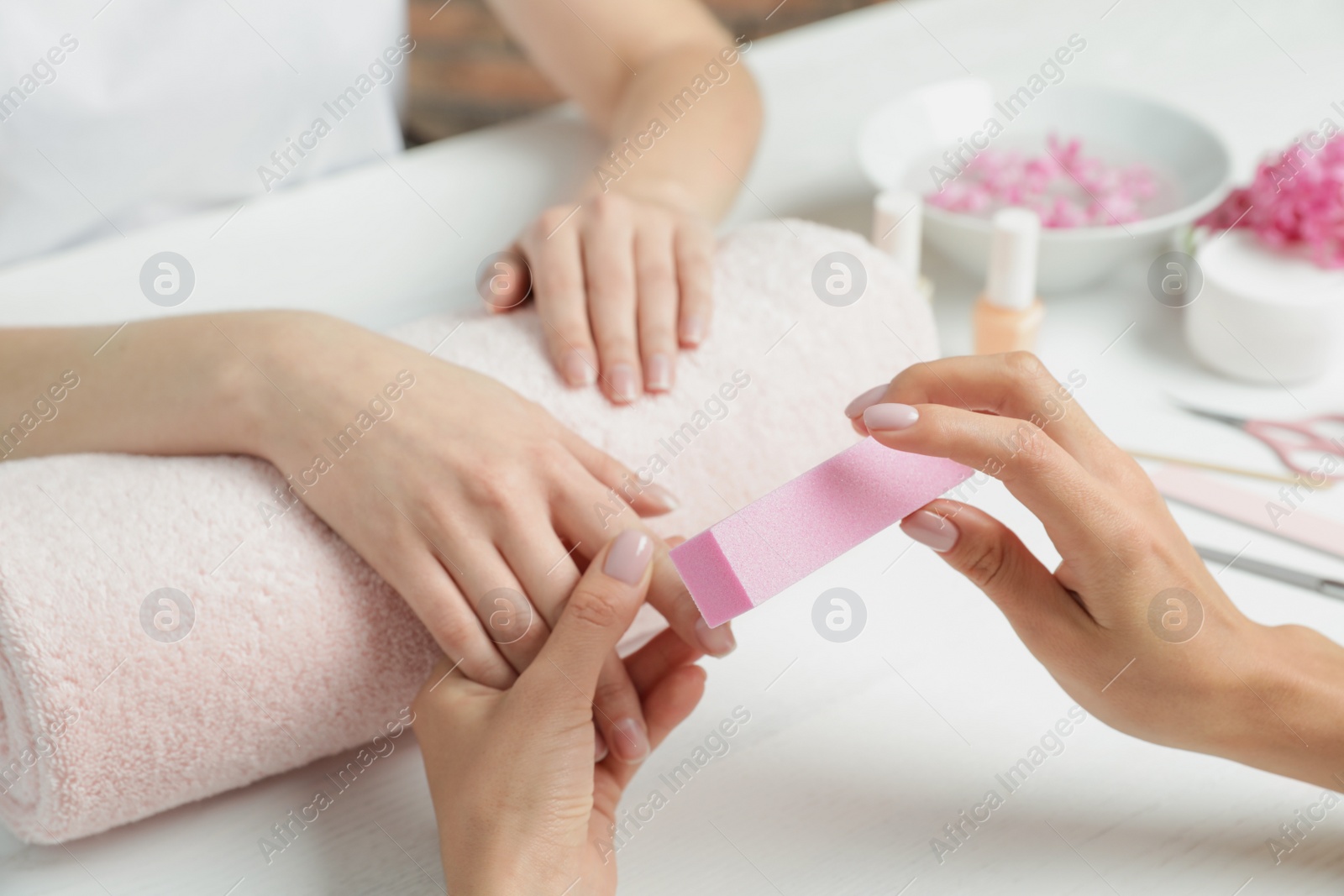 Photo of Manicurist polishing client's nails with buffer at table, closeup. Spa treatment