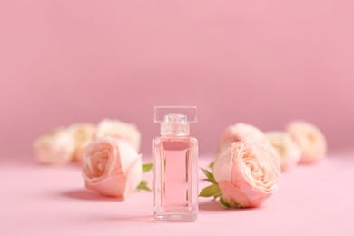 Photo of Bottle of perfume with beautiful roses on color background