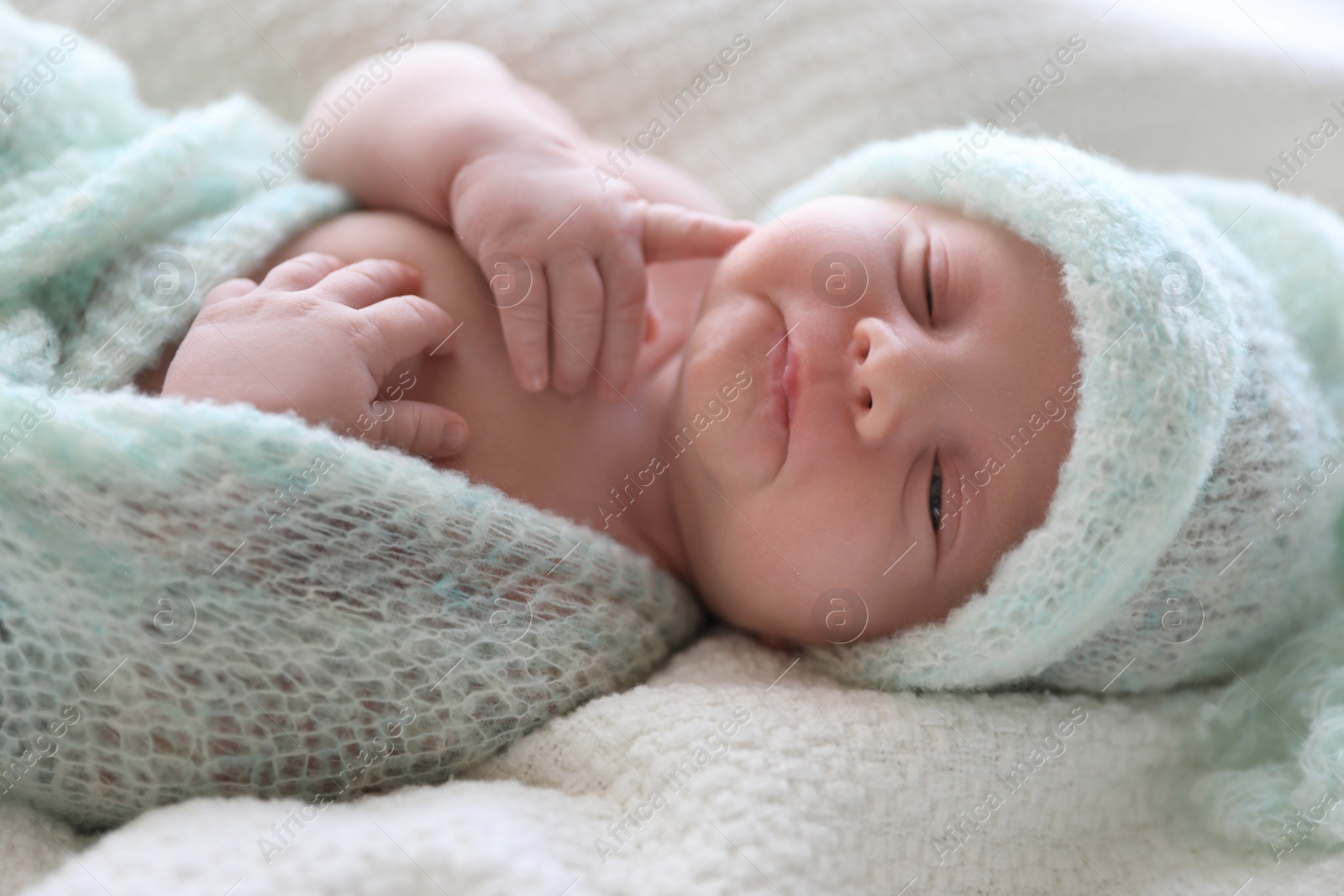 Photo of Cute newborn baby in warm hat lying on white plaid, closeup