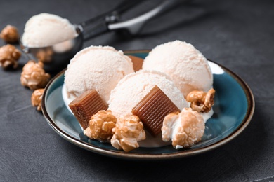 Plate of ice cream with caramel candies and popcorn on grey table
