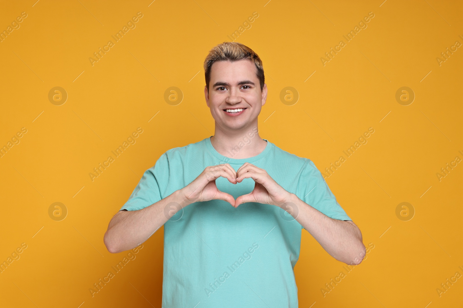 Photo of Young man showing heart gesture with hands on orange background