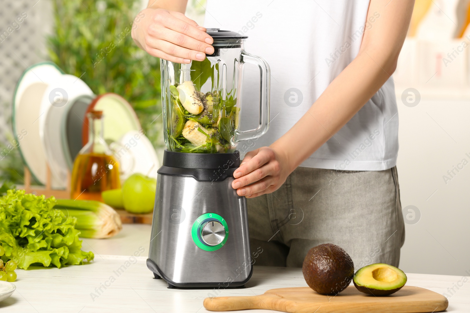 Photo of Woman preparing tasty green smoothie at white wooden table in kitchen, closeup