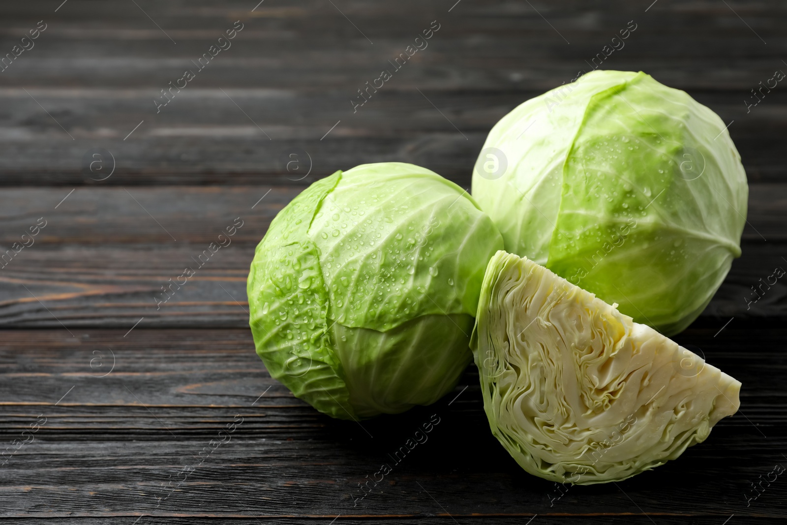 Photo of Ripe white cabbage with water drops on black wooden table