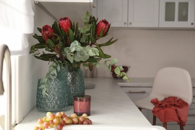 Photo of Bouquet with beautiful protea flowers on countertop in kitchen. Interior design