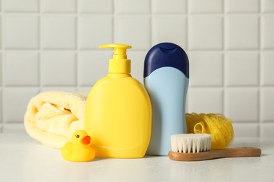 Baby cosmetic products, bath duck, brush and towel on white table against tiled wall