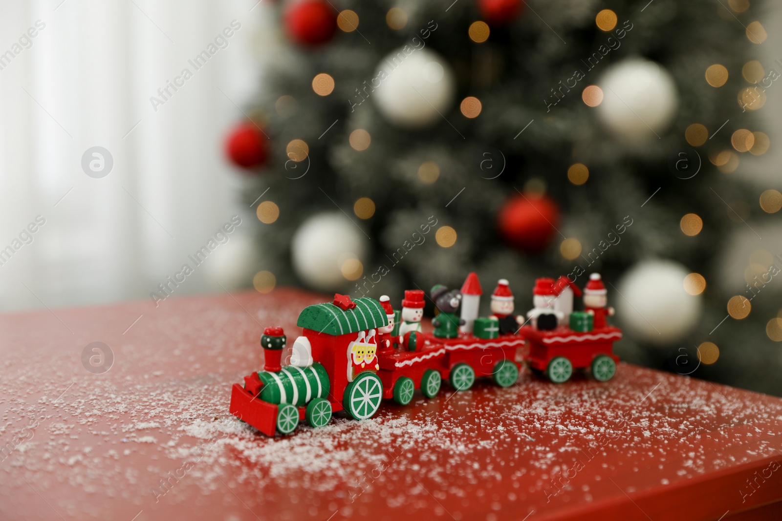 Photo of Bright toy train on table in room with Christmas tree