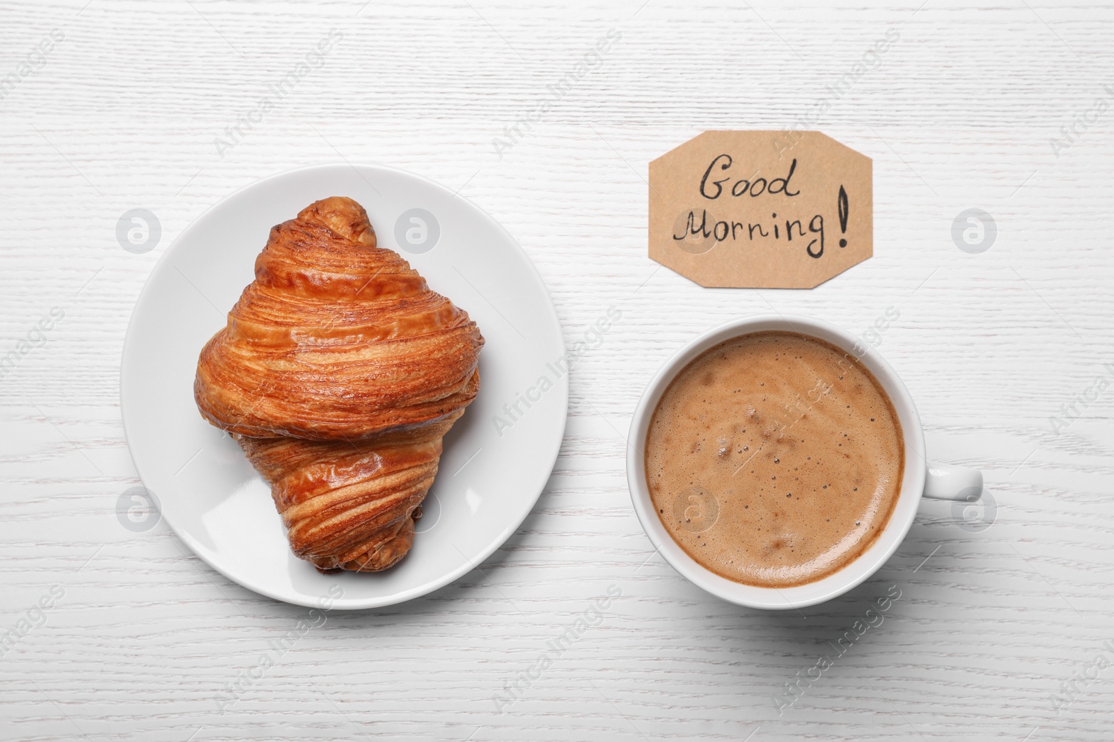 Photo of Aromatic coffee, croissant and Good Morning! message on white wooden table, flat lay