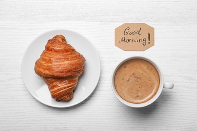 Aromatic coffee, croissant and Good Morning! message on white wooden table, flat lay