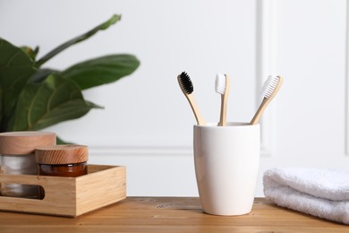 Photo of Bamboo toothbrushes in holder, towel, cosmetic products and leaves on wooden table