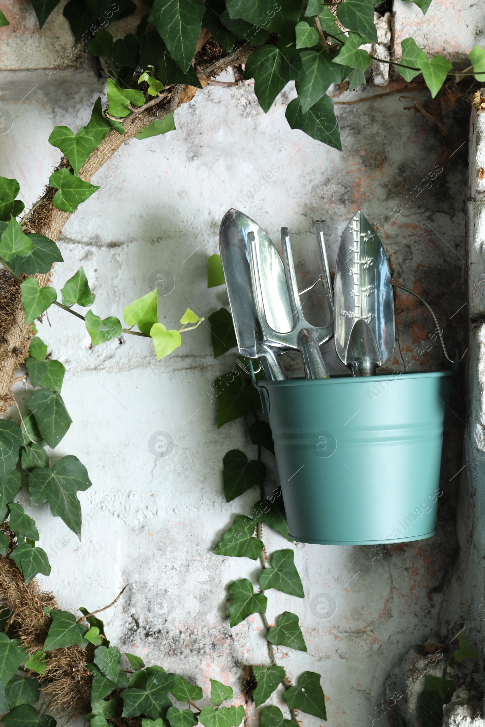 Photo of Bucket with shovels and rake on white wall outdoors. Gardening tools