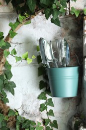 Photo of Bucket with shovels and rake on white wall outdoors. Gardening tools