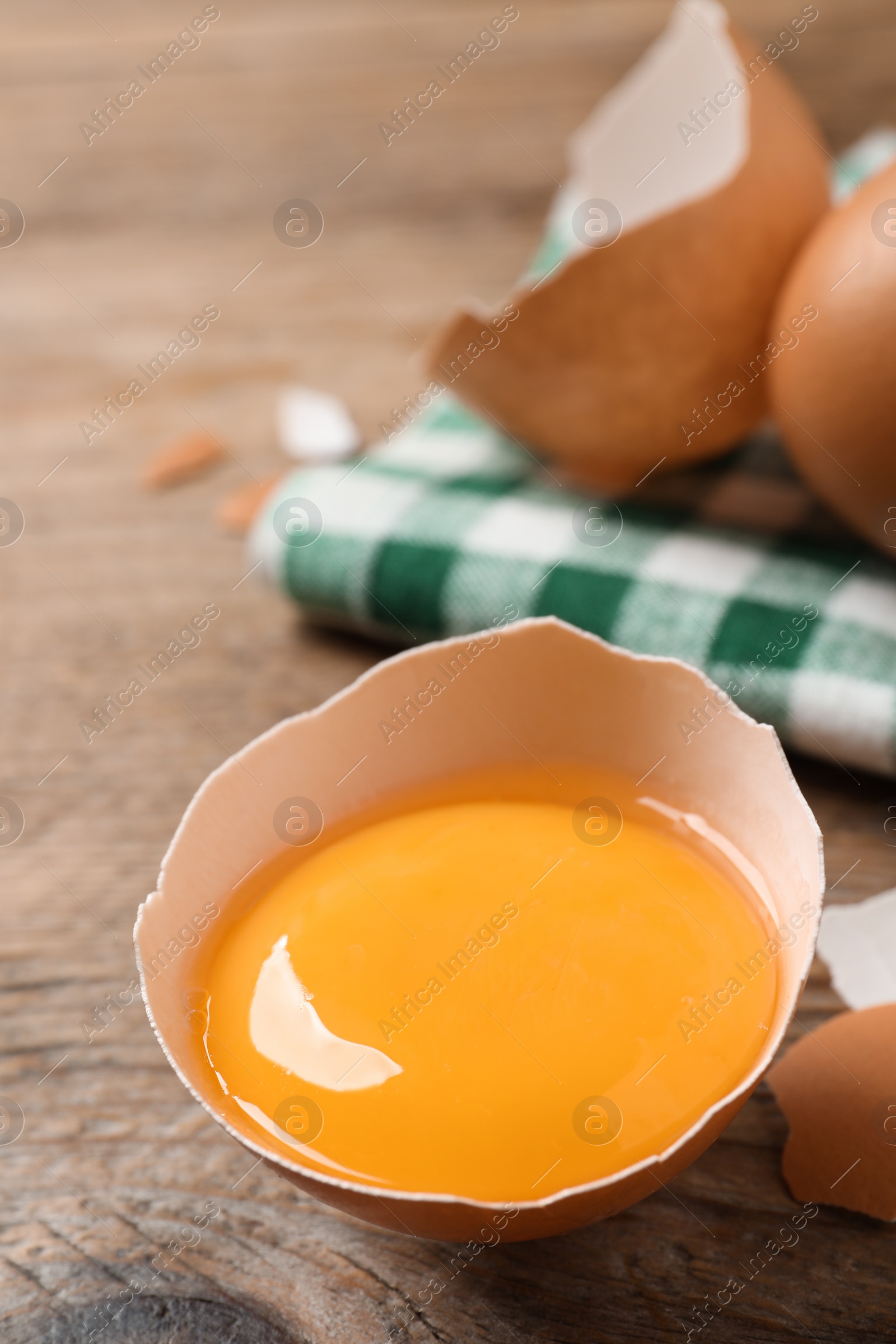 Photo of Cracked raw chicken egg with yolk on wooden table, closeup