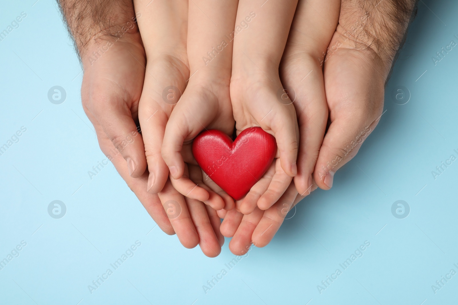 Photo of Parents and kid holding red heart in hands on light blue background, top view