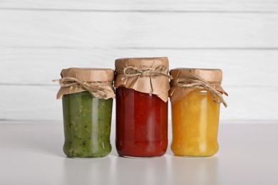 Photo of Jars with canned fruit jams on light grey table