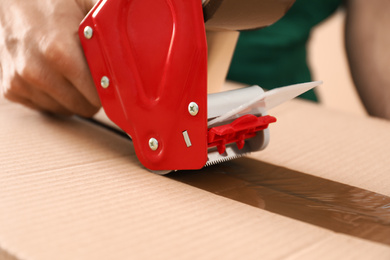Photo of Man packing box with adhesive tape, closeup. Moving service