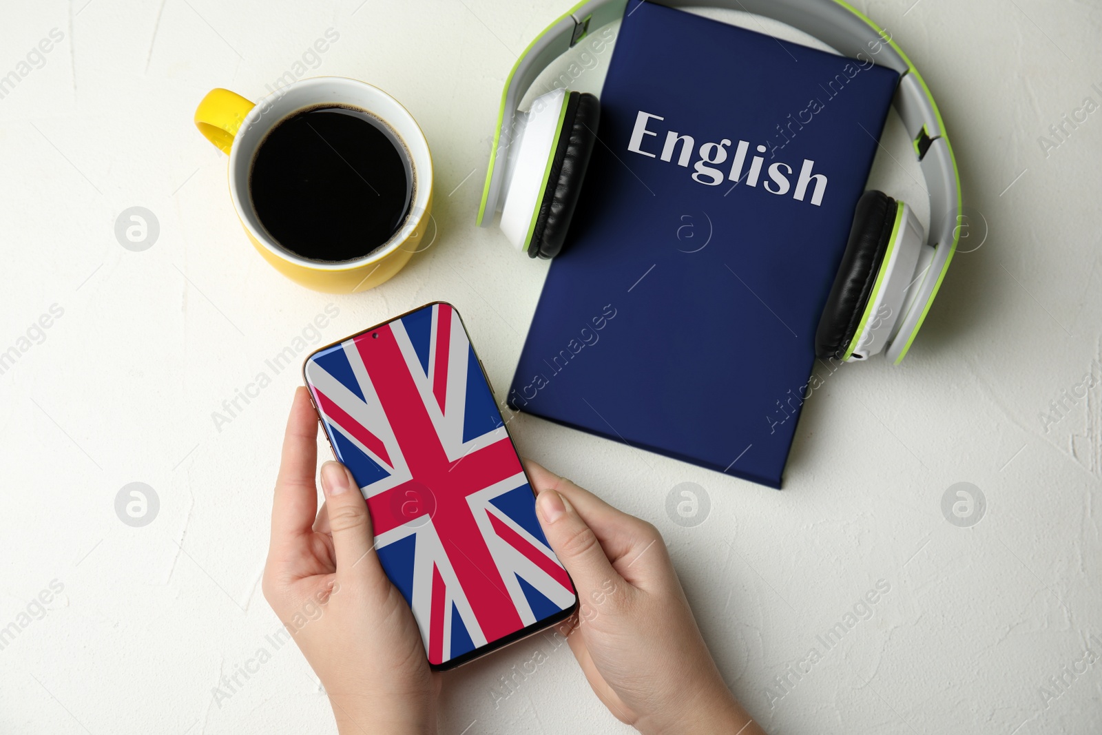 Image of Woman holding mobile phone over white stone table with book, top view. Learning English