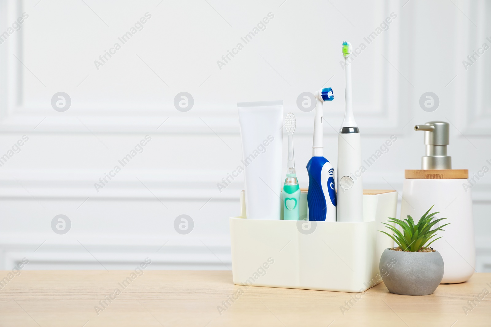 Photo of Electric toothbrushes and soap dispenser on wooden table. Space for text