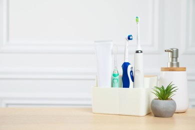 Electric toothbrushes and soap dispenser on wooden table. Space for text