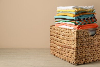 Photo of Wicker laundry basket with clean clothes on floor near beige wall. Space for text