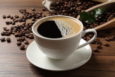 Photo of Cup of aromatic hot coffee and beans on wooden table, closeup