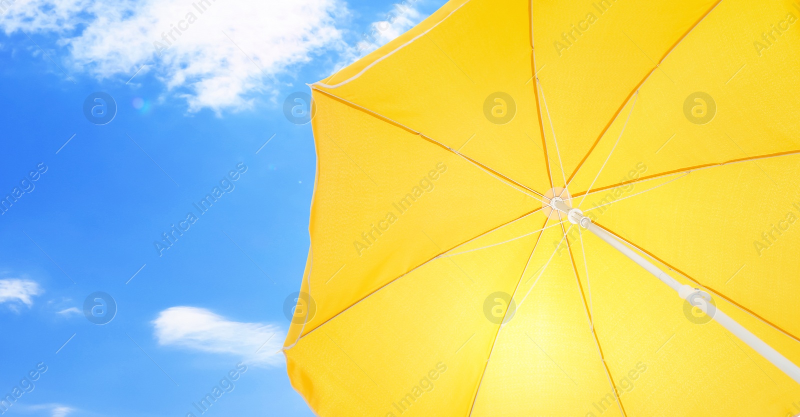 Image of Open big yellow beach umbrella and beautiful blue sky with white clouds on background