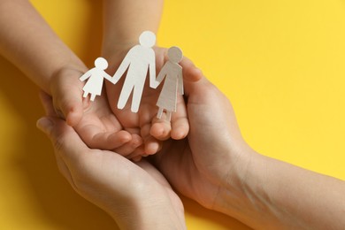 Photo of Mother and child holding paper cutout of family on yellow background, closeup