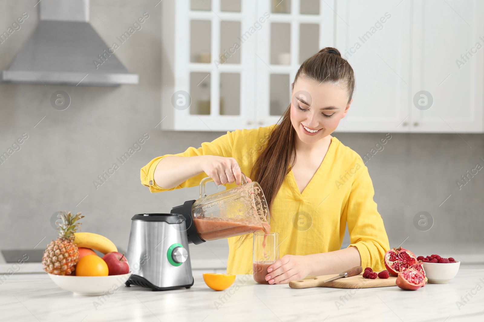 Photo of Woman pouring tasty smoothie into glass at white table in kitchen