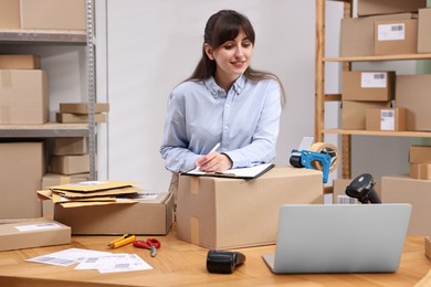 Photo of Parcel packing. Post office worker with clipboard writing notes at wooden table indoors