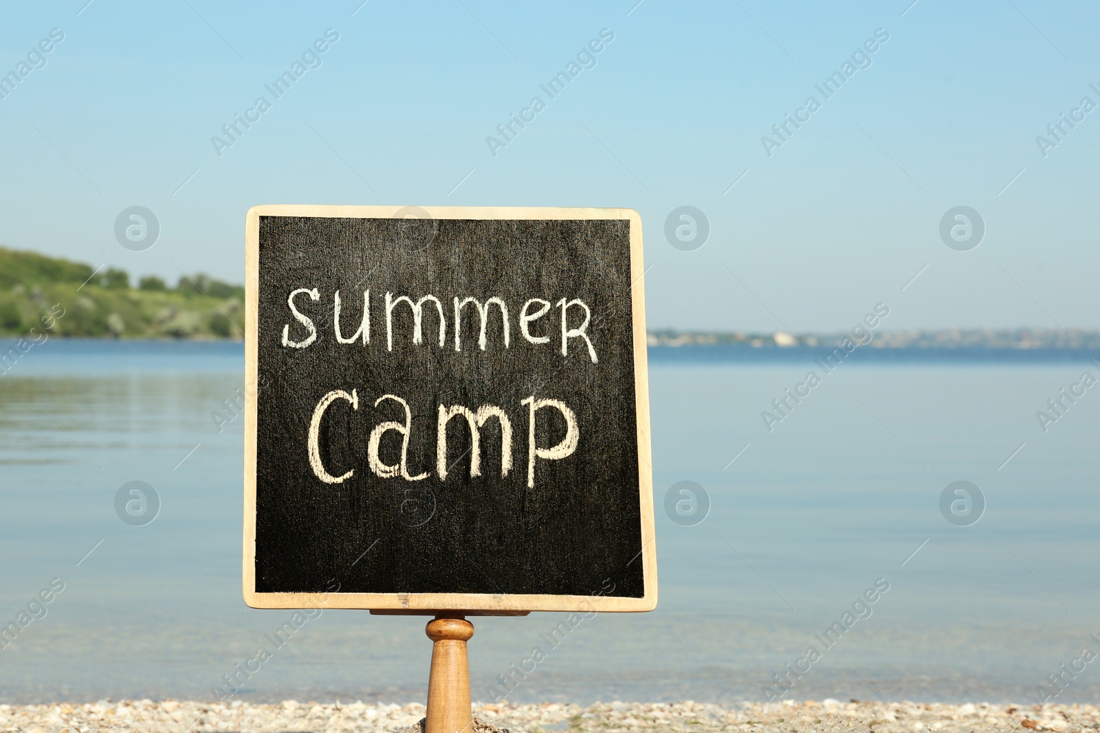 Photo of Small chalkboard with text SUMMER CAMP on beach near river