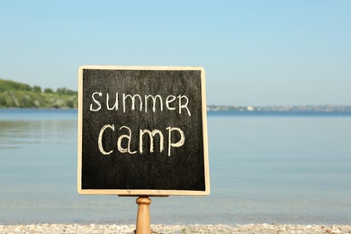 Photo of Small chalkboard with text SUMMER CAMP on beach near river